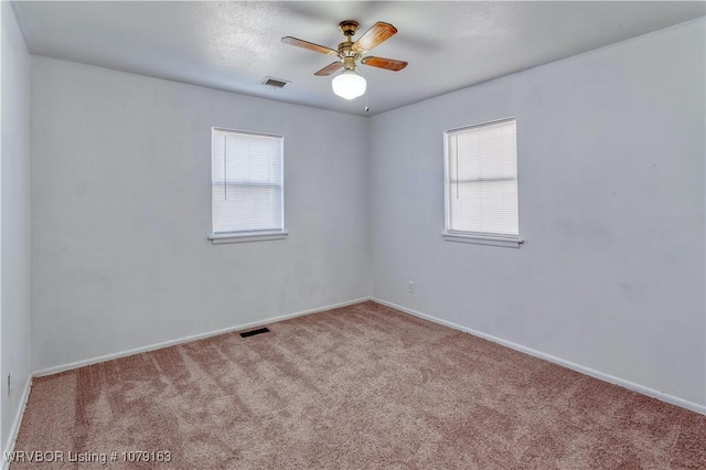 empty room with carpet floors, visible vents, baseboards, and a ceiling fan