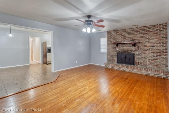 unfurnished living room with a brick fireplace, ceiling fan, baseboards, and hardwood / wood-style flooring