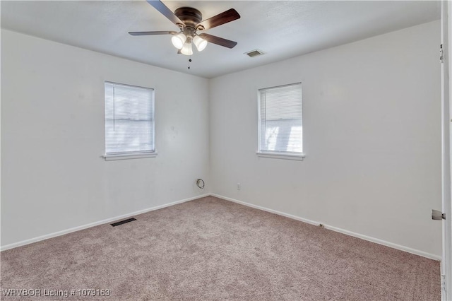 carpeted spare room featuring ceiling fan, visible vents, and baseboards