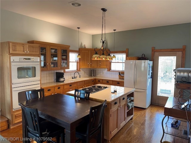 kitchen with light countertops, decorative backsplash, wood finished floors, white appliances, and a sink