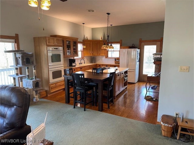 kitchen with white appliances, backsplash, a sink, light countertops, and a wealth of natural light