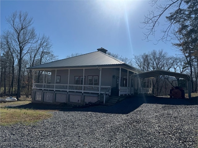 exterior space featuring metal roof, gravel driveway, a carport, and a porch