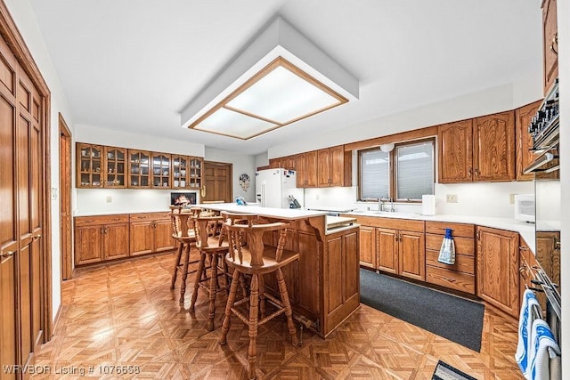 kitchen featuring a kitchen bar, sink, light parquet flooring, a kitchen island, and white fridge with ice dispenser