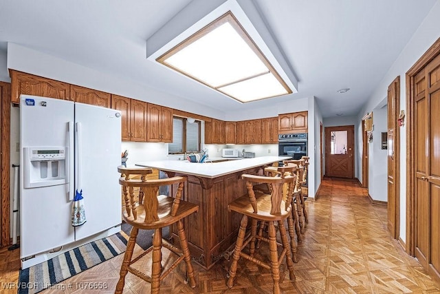 kitchen featuring kitchen peninsula, white appliances, a breakfast bar area, and light parquet floors