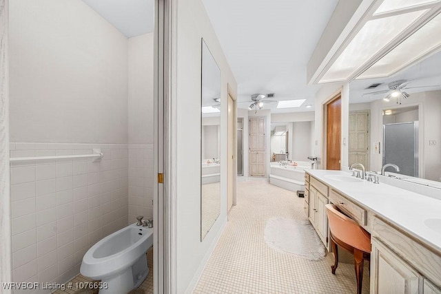 bathroom featuring a skylight, tile patterned flooring, a bidet, vanity, and tile walls