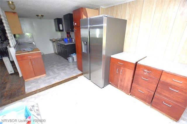 kitchen featuring a textured ceiling, light countertops, wooden walls, light floors, and stainless steel refrigerator with ice dispenser