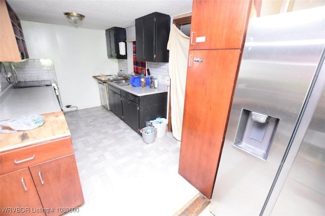 kitchen featuring light floors, decorative backsplash, light countertops, a sink, and stainless steel refrigerator with ice dispenser