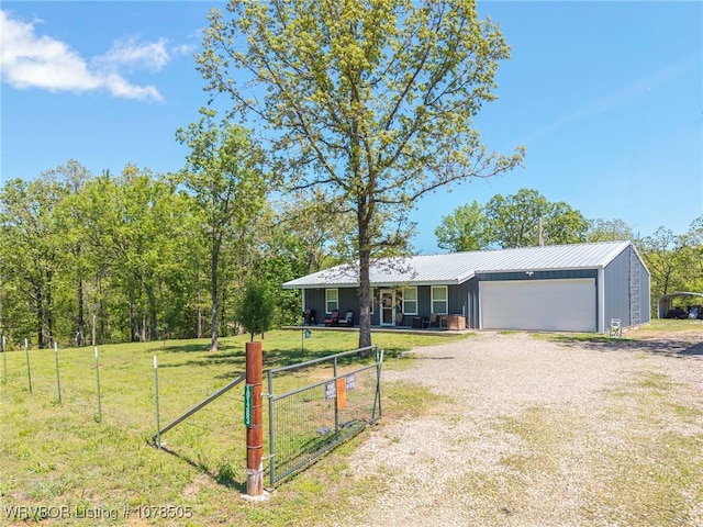 ranch-style home featuring board and batten siding, gravel driveway, metal roof, a front lawn, and an attached garage
