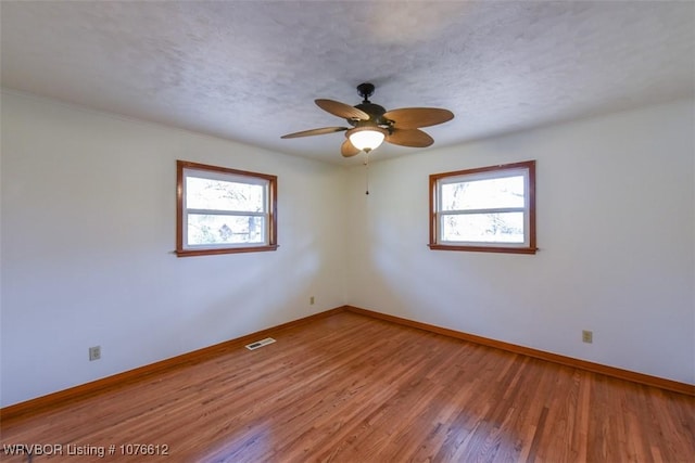 empty room with hardwood / wood-style floors, a textured ceiling, ceiling fan, and a healthy amount of sunlight