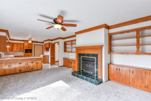 living room with ceiling fan, sink, crown molding, light colored carpet, and a tiled fireplace