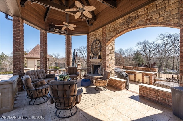 view of patio / terrace with exterior kitchen, an outdoor stone fireplace, and fence