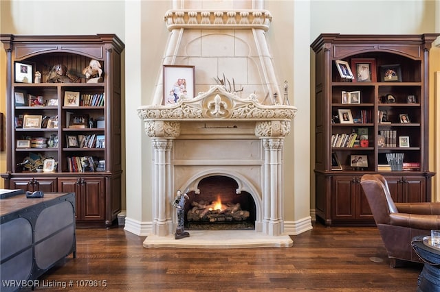 living room featuring dark wood-type flooring, baseboards, and a lit fireplace