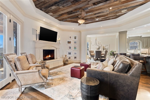 living room with ceiling fan, a tray ceiling, crown molding, and a lit fireplace