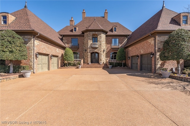 french provincial home with brick siding, driveway, a chimney, and a garage