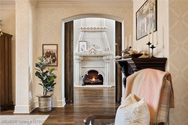 sitting room featuring wood finished floors, baseboards, wallpapered walls, a warm lit fireplace, and crown molding