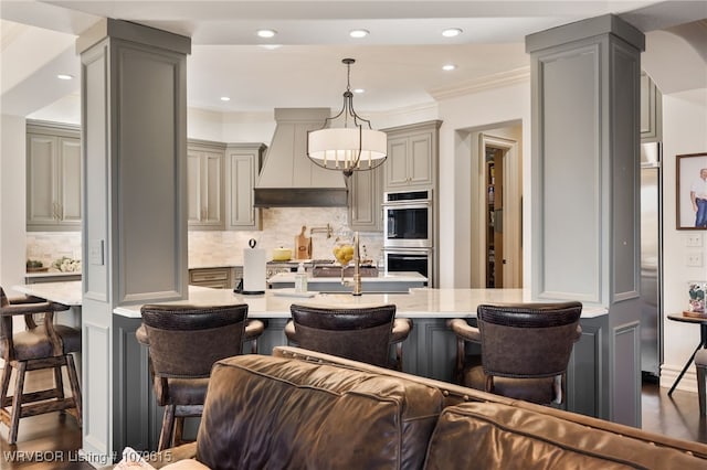 kitchen with custom exhaust hood, gray cabinetry, stainless steel appliances, and a kitchen bar