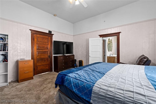 bedroom featuring carpet flooring, ceiling fan, wood walls, and ensuite bath