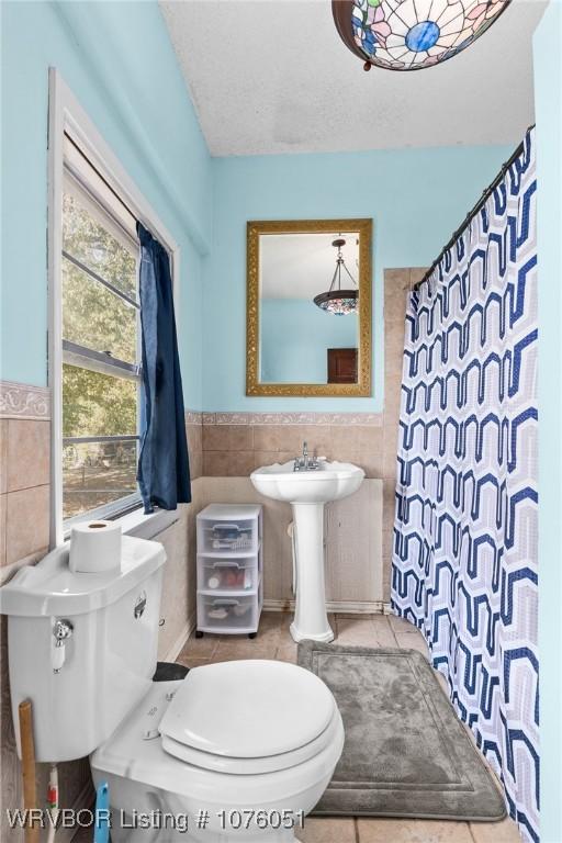 bathroom with tile patterned floors, walk in shower, a textured ceiling, tile walls, and toilet