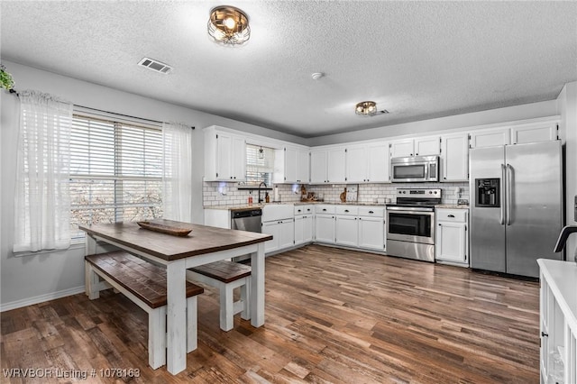 kitchen featuring dark hardwood / wood-style flooring, tasteful backsplash, a textured ceiling, stainless steel appliances, and white cabinetry