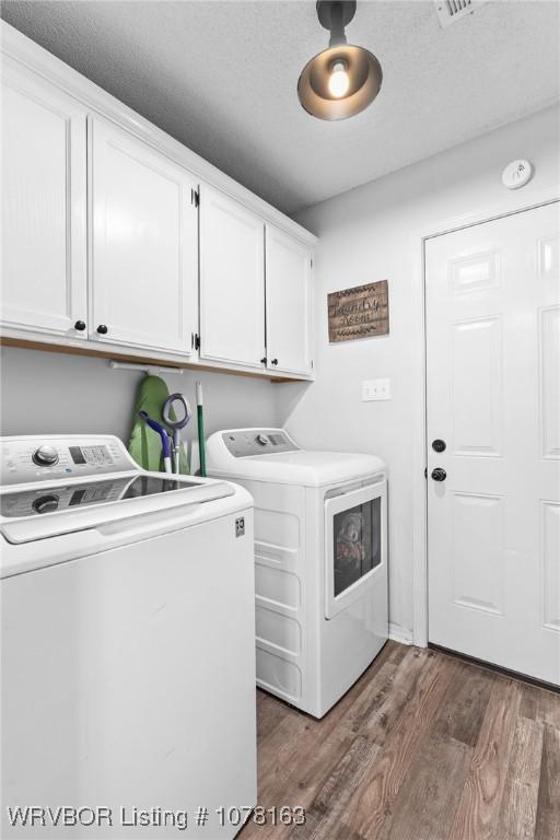 laundry area featuring washing machine and clothes dryer, dark wood-type flooring, cabinets, and a textured ceiling