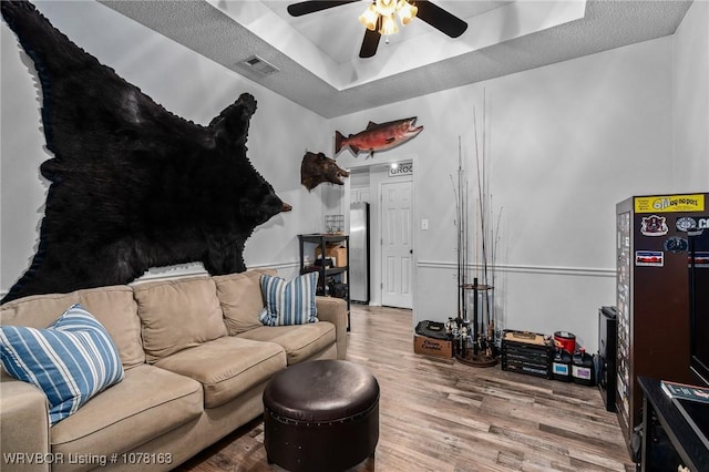 living room featuring ceiling fan, wood-type flooring, and a tray ceiling