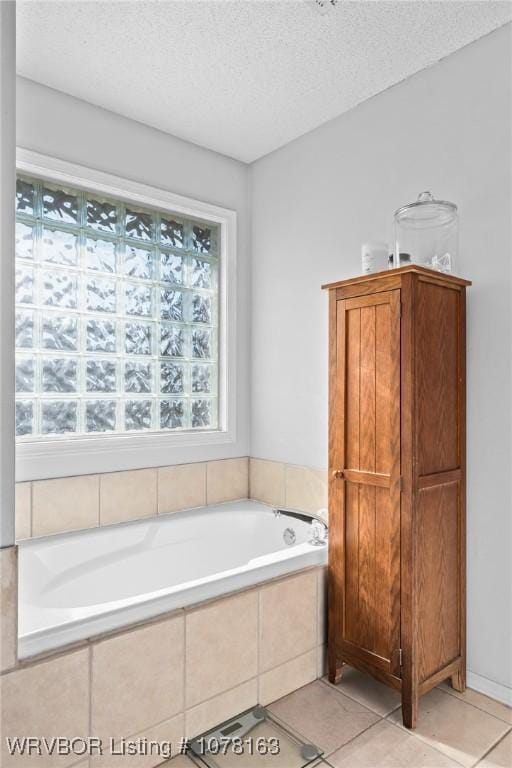 bathroom with tile patterned flooring, a relaxing tiled tub, a textured ceiling, and a wealth of natural light