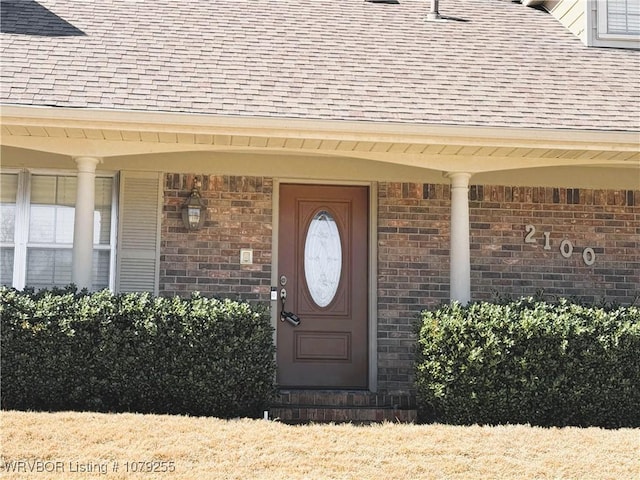 property entrance featuring brick siding and roof with shingles