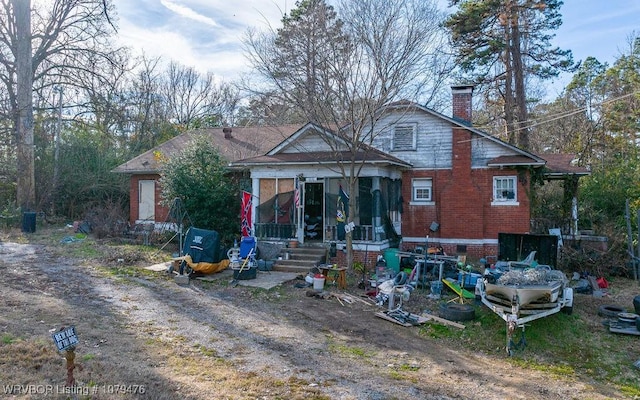 back of house with brick siding, a chimney, and a sunroom