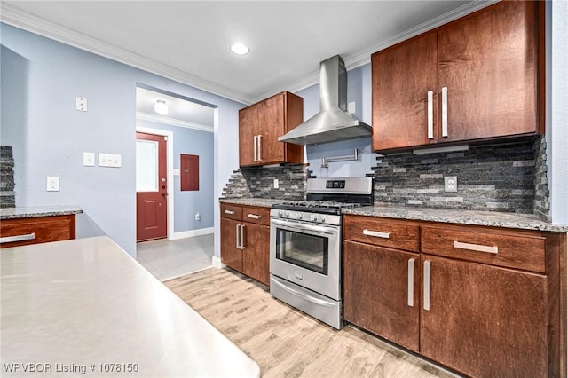 kitchen with stainless steel range with gas cooktop, crown molding, wall chimney range hood, decorative backsplash, and light hardwood / wood-style floors