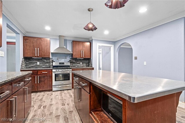 kitchen featuring wall chimney range hood, backsplash, pendant lighting, a kitchen island, and appliances with stainless steel finishes