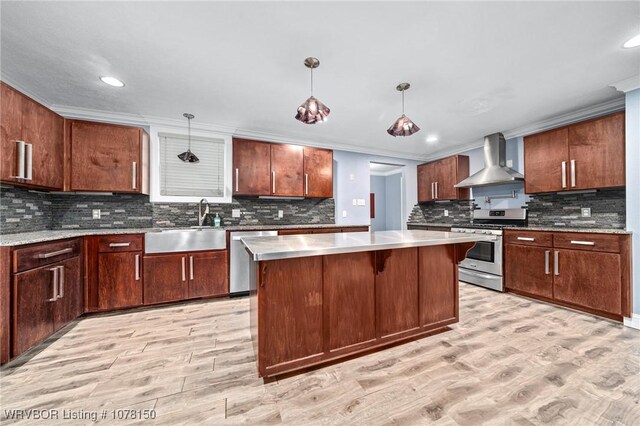 kitchen featuring stainless steel appliances, crown molding, wall chimney range hood, a center island, and hanging light fixtures