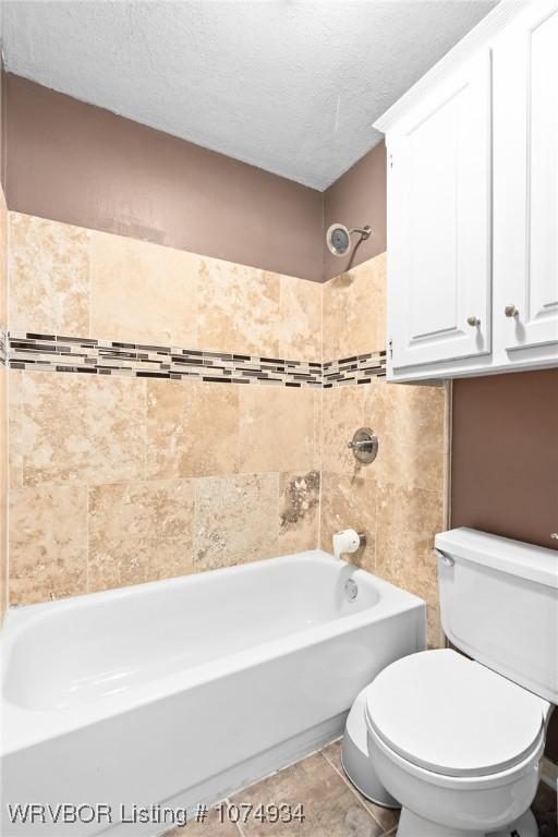 bathroom featuring tile patterned flooring, tiled shower / bath, a textured ceiling, and toilet