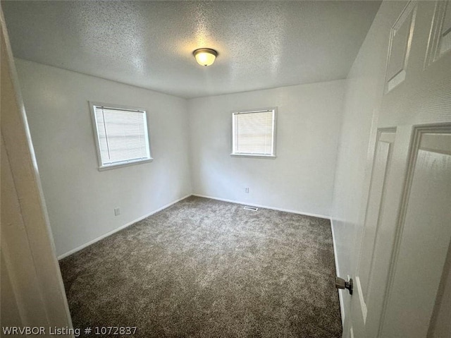 unfurnished room featuring plenty of natural light, a textured ceiling, and dark colored carpet