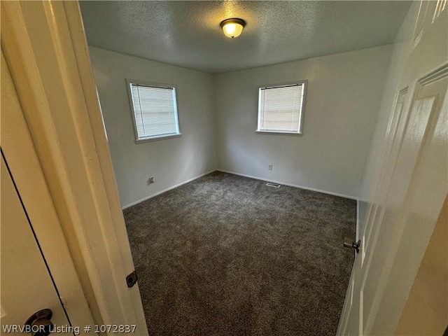 spare room with dark colored carpet, plenty of natural light, and a textured ceiling