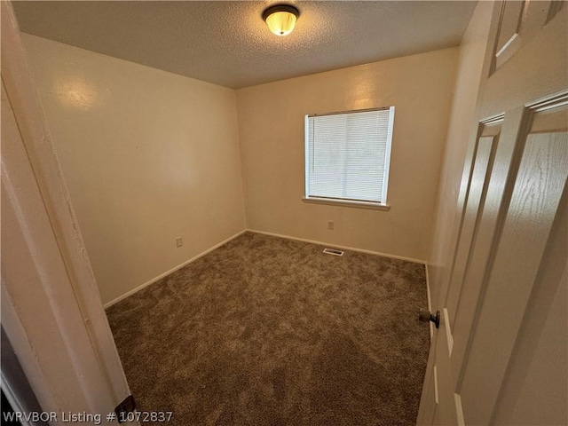 spare room featuring a textured ceiling and dark colored carpet