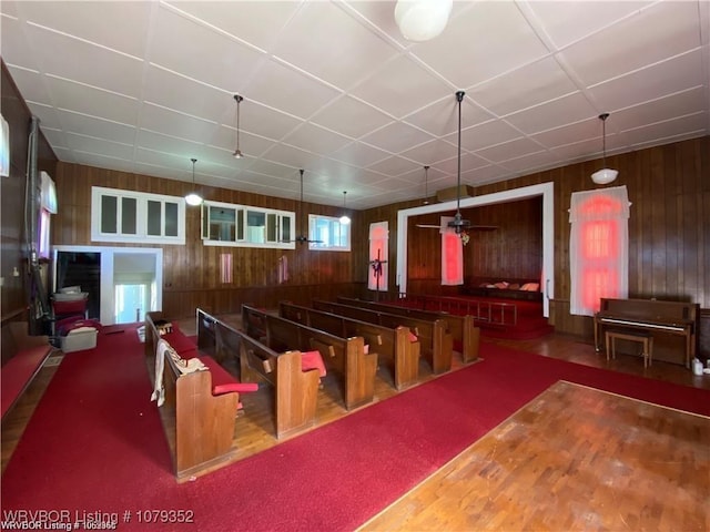 interior space with a paneled ceiling, wooden walls, and a ceiling fan