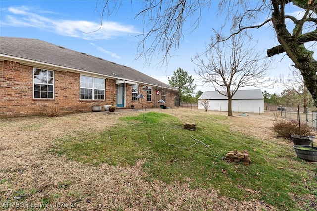 rear view of property featuring roof with shingles, an outdoor structure, a lawn, and brick siding