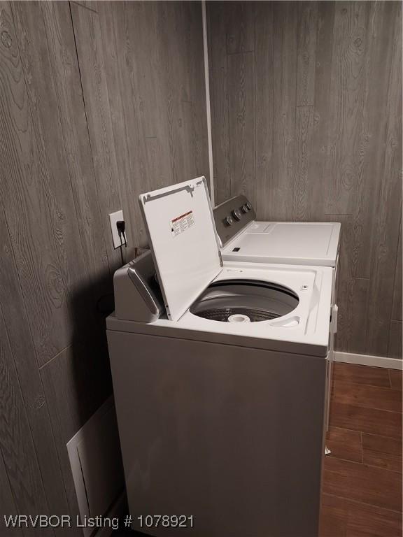 clothes washing area with dark hardwood / wood-style flooring, wooden walls, and washing machine and clothes dryer