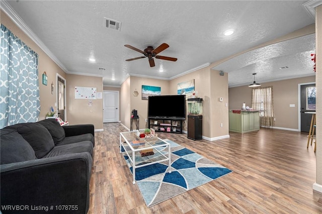 living room featuring ceiling fan, ornamental molding, wood-type flooring, and a textured ceiling