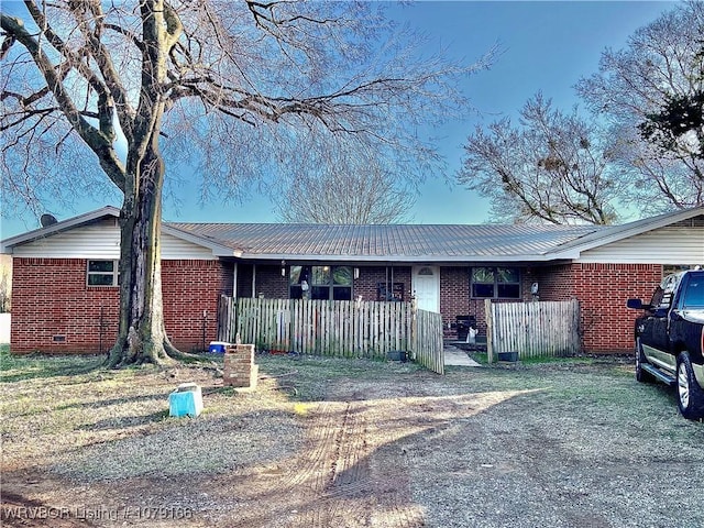 ranch-style home featuring metal roof, brick siding, and fence