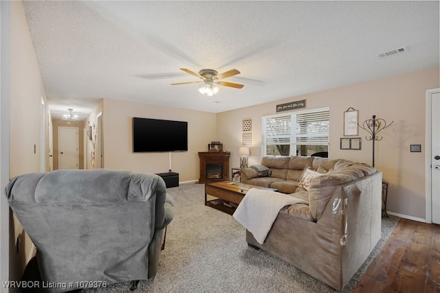 living room with baseboards, visible vents, a ceiling fan, a textured ceiling, and a fireplace