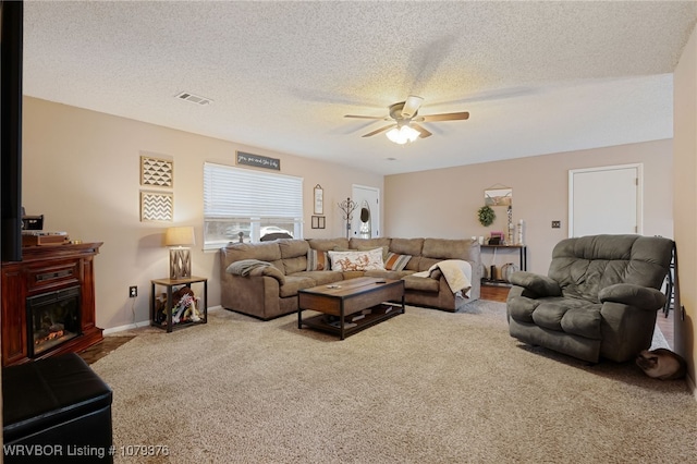 living area with carpet, visible vents, a ceiling fan, a glass covered fireplace, and a textured ceiling