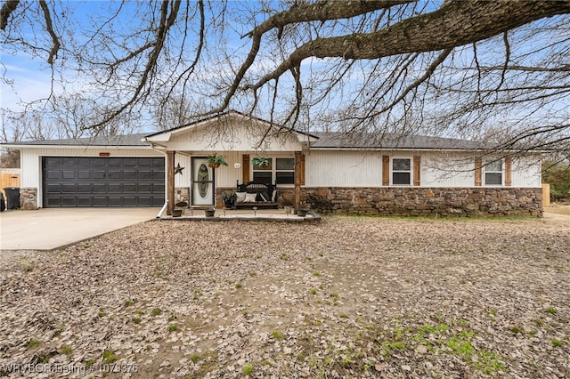 ranch-style house featuring an attached garage, stone siding, covered porch, and concrete driveway