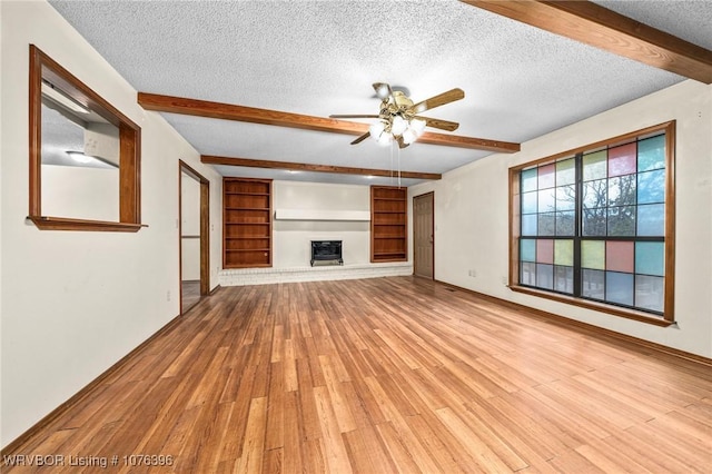 unfurnished living room with built in shelves, ceiling fan, light hardwood / wood-style flooring, beamed ceiling, and a textured ceiling