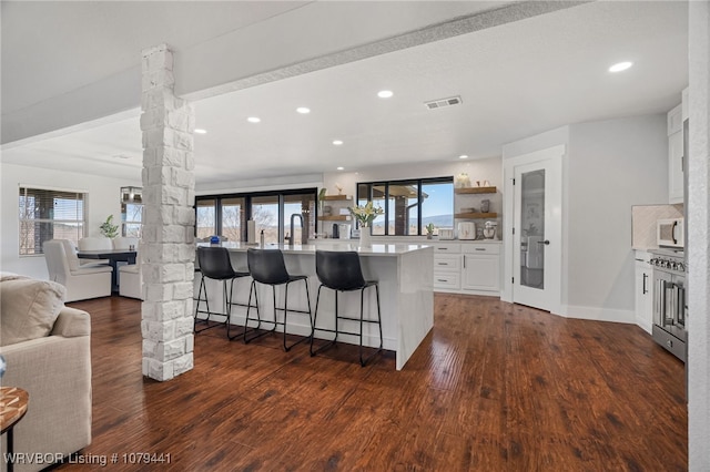 kitchen with decorative columns, open shelves, visible vents, white microwave, and open floor plan