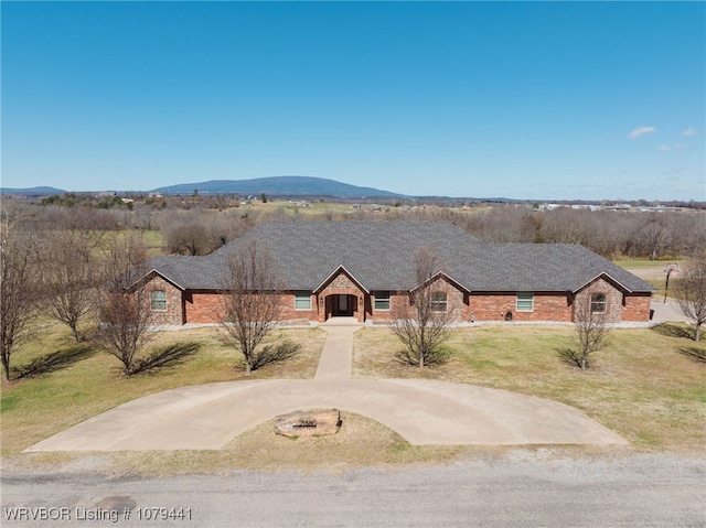 view of front facade with brick siding, a shingled roof, concrete driveway, a front yard, and a mountain view