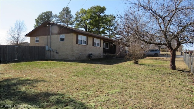 view of side of property featuring brick siding, fence, and a lawn