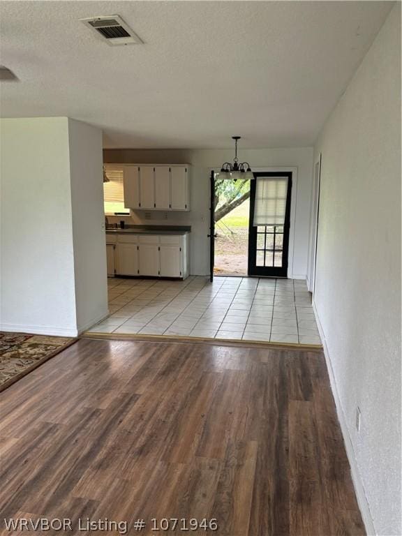 unfurnished living room with a notable chandelier, light wood-type flooring, and a textured ceiling