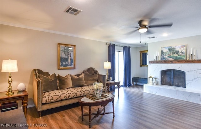 living area featuring wood finished floors, a ceiling fan, visible vents, and a fireplace with raised hearth