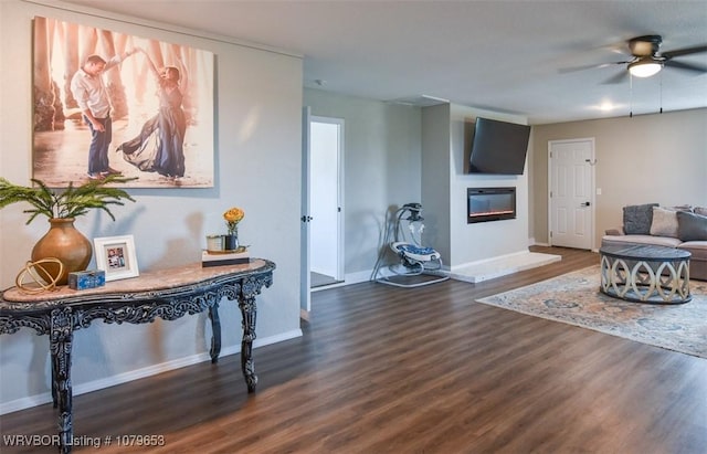 interior space featuring a glass covered fireplace, wood finished floors, baseboards, and ceiling fan